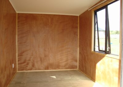 Unfurnished cabin interior with an awning window looking out to open farmland