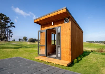 Cedar-clad OutaSpace cabin on a lawn with its glass door open