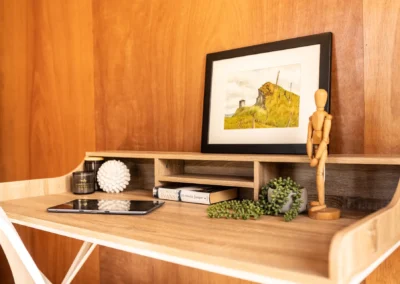 Cabin desk with framed print, wooden artist figure and storage shelf above