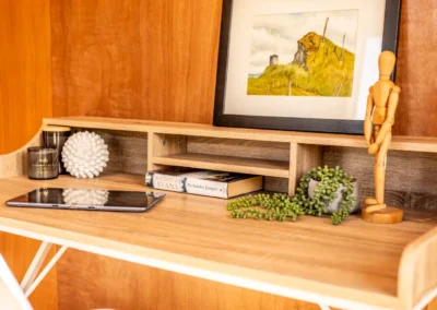 Desk inside an OutaSpace cabin with framed artwork, shelf and a small potted plant