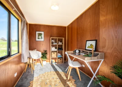 Cabin interior furnished as a home office, with a desk, chair and window looking out over paddocks